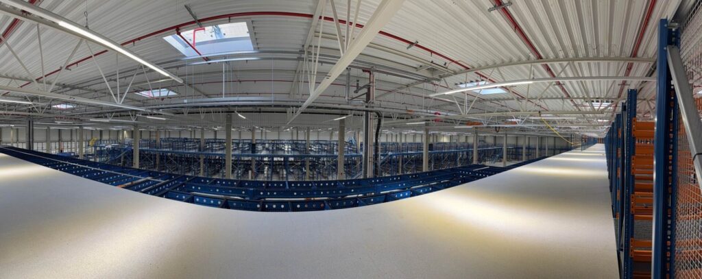 Panoramiczny widok magazynu z systemem regałów, ukazujący przestronność obiektu, co jest kluczowe przy obliczaniu pojemności magazynu i efektywnym wykorzystaniu dostępnej przestrzeni do składowania towarów - rozwiązania Nedcon